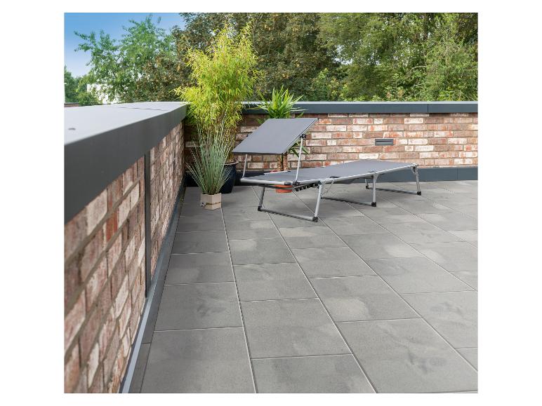 Graue Sonnenliege auf einem gefliesten Balkon mit Ziegelwänden und Pflanzen.