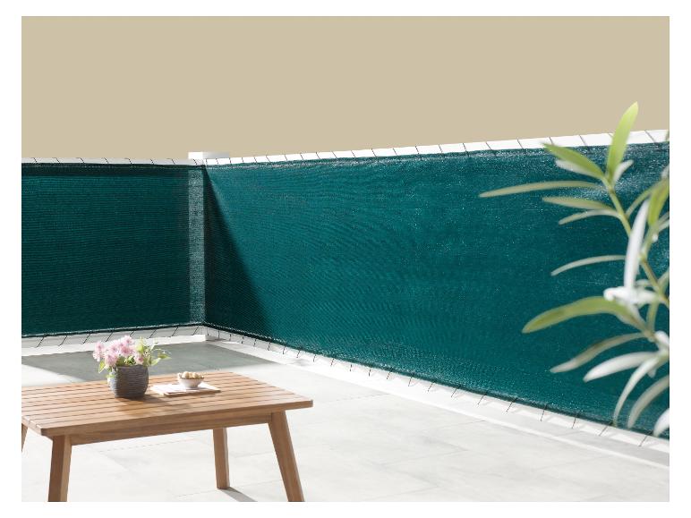 Dunkelgrüner Balkon-Sichtschutz, mit einem Holztisch und Topfblumen.