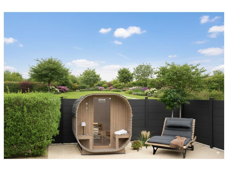 Außensauna HOME DELUXE und Sonnenliege in einem Garten mit Rasen und Blumen.
