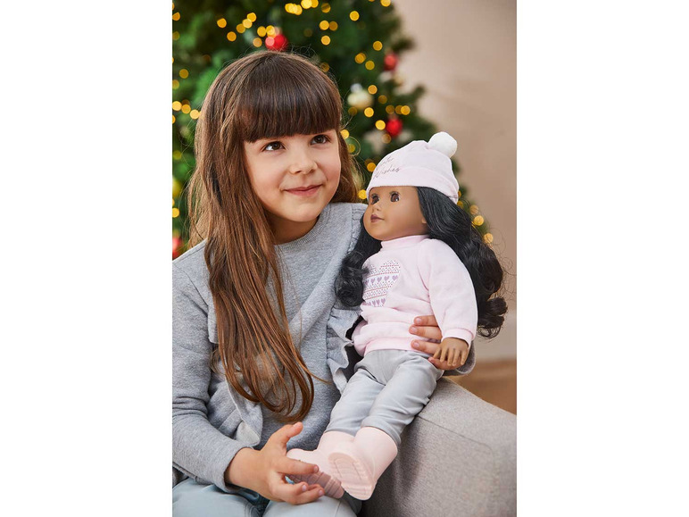 Ein Mädchen hält eine Puppe mit einem Weihnachtspullover und einer Mütze.