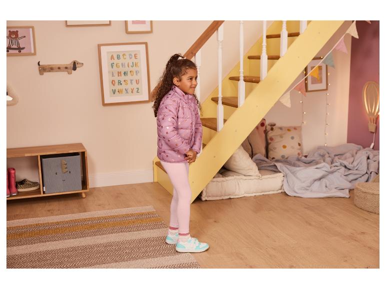 Mädchen in lila Jacke und rosa Leggings steht in einem Kinderzimmer mit Treppe.
