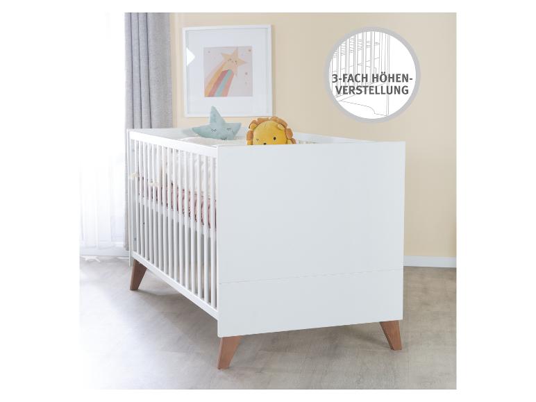 Weißes Babybett mit Holzbeinen, mit einem Löwenspielzeug und einem Sternenkissen.