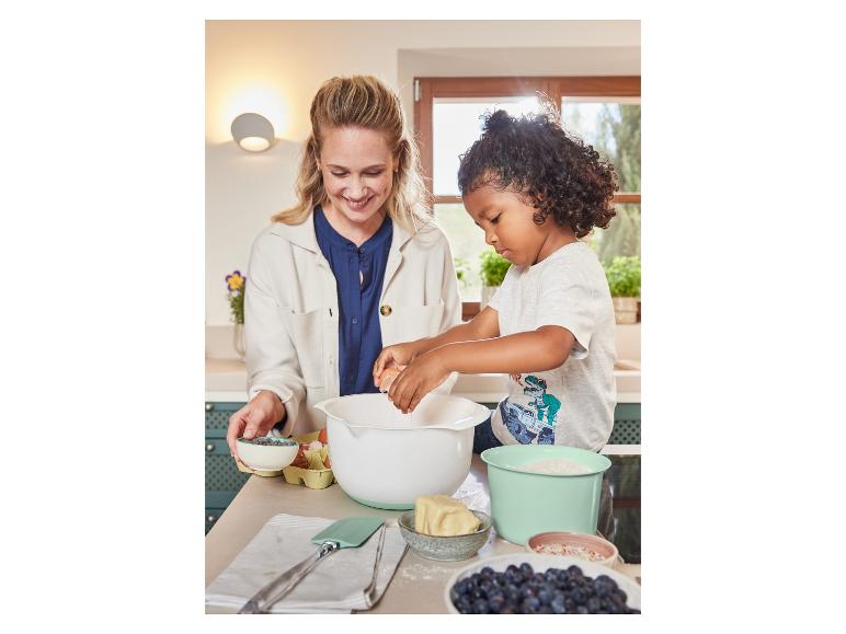 Ein Erwachsener und ein Kind backen zusammen mit einer Rührschüssel und anderen Backutensilien.