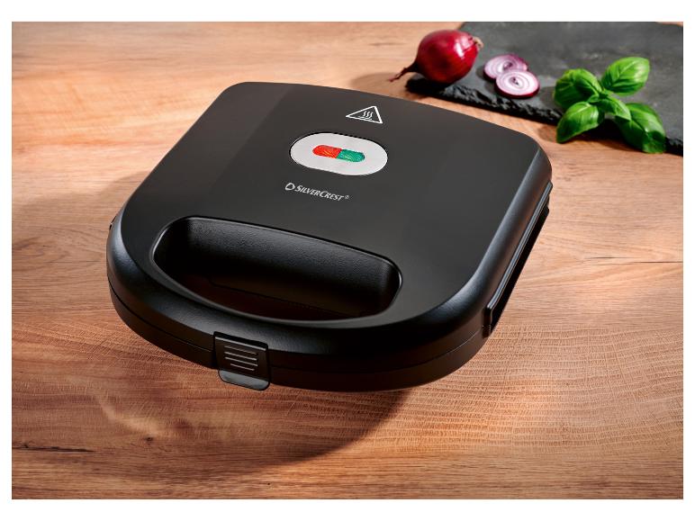 Schwarzer SilverCrest Sandwichmaker auf einem Holztisch mit Zwiebel und Basilikum.