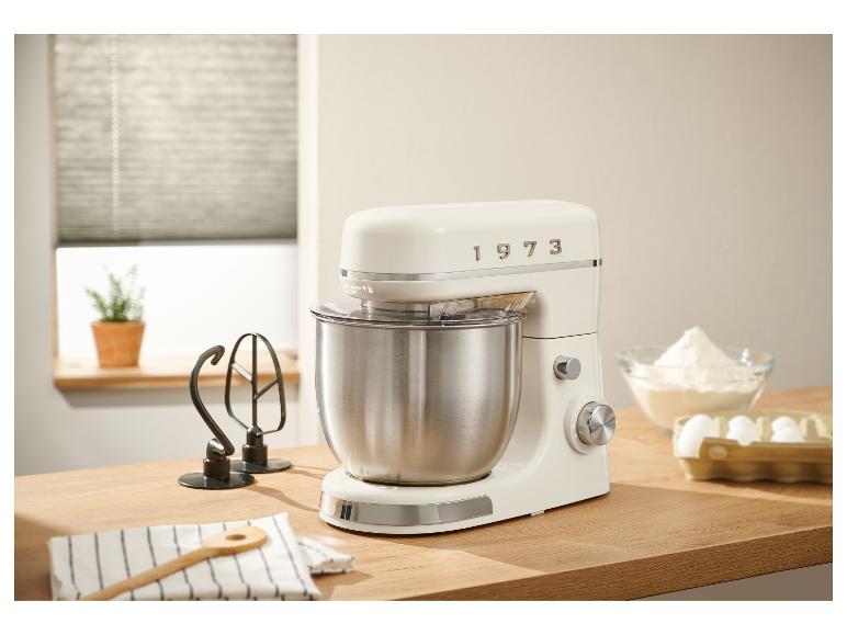 Ein cremefarbener Küchenmixer im Stil der 1970er Jahre steht auf einer Holztheke, umgeben von Backzutaten.