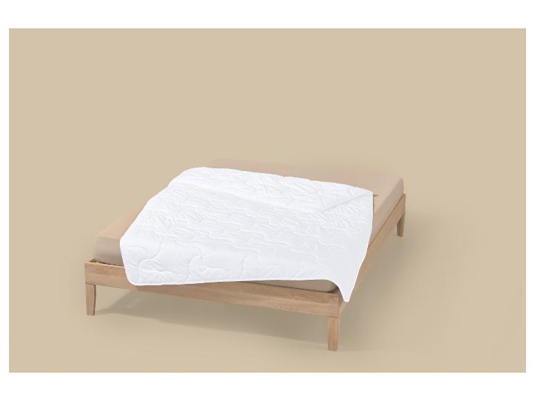 Weiße Bettdecke auf einem Holzrahmenbett mit beiger Bettwäsche.