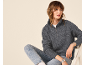 Frau in grauem Reißverschluss-Pullover und Jeans, auf einem Stuhl sitzend.