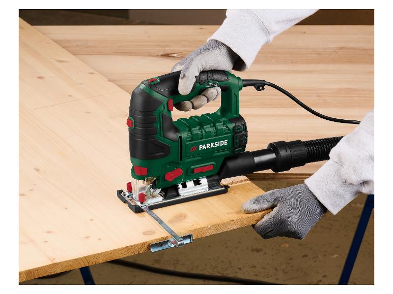 Eine Person schneidet ein Holzbrett mit einer elektrischen Stichsäge und trägt Schutzhandschuhe.