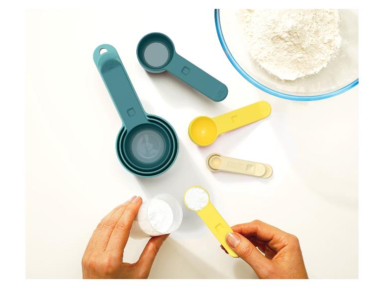 Ein Satz Messbecher und -löffel, mit einer Schüssel Mehl und einer Hand, die einen Löffel mit Pulver hält.