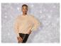 Eine Frau trägt einen beigefarbenen Pullover mit glitzernden Details und eine schwarze Lederhose.