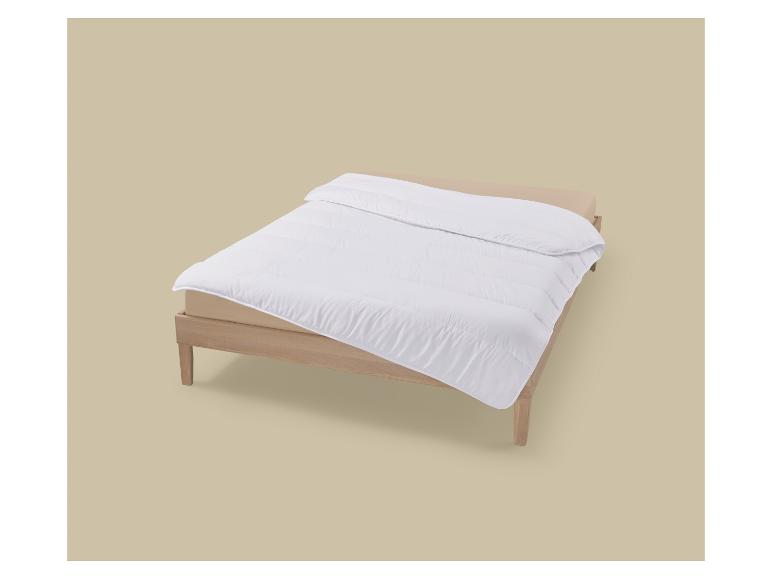 Weiße Bettdecke auf einem Holzrahmenbett mit beigem Laken.