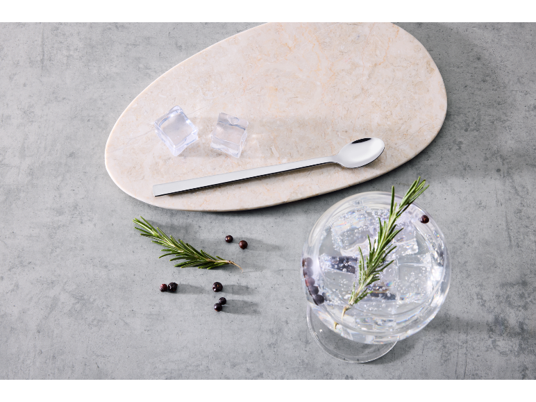 Gin Tonic mit Rosmarin und Wacholderbeeren, Eiswürfeln und einem langen Löffel.