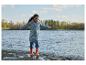 Kind in Regenmantel und Stiefeln spielt am Wasser.