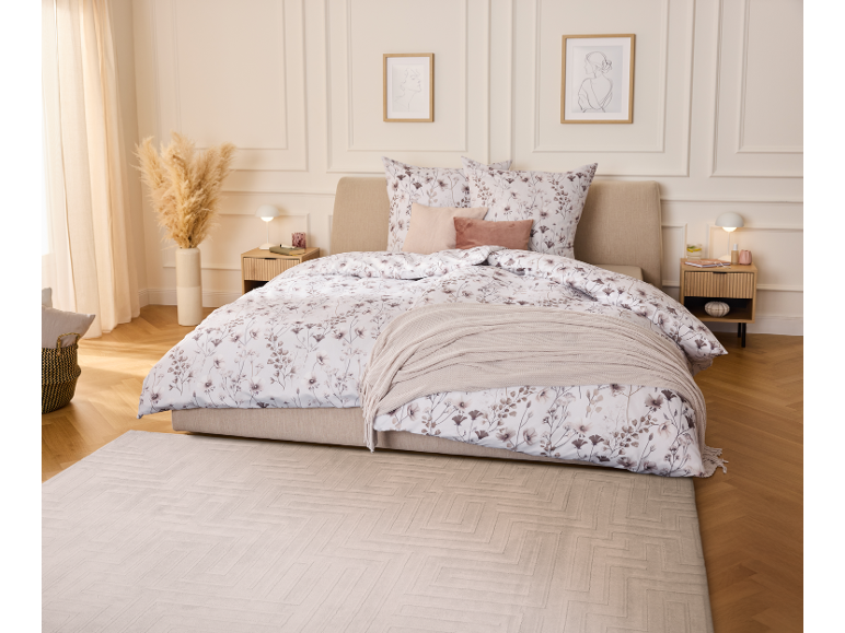 Schlafzimmer mit Bett mit floraler Bettwäsche, zwei Nachttischen und einem Teppich.