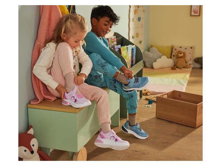 Zwei Kinder probieren ihre neuen Sneaker aus: ein rosa mit Einhorn und ein blauer mit Bagger.