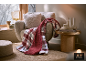 Gemütlicher Sessel mit einer weichen Karo-Decke und Zierkissen im Wohnzimmer.