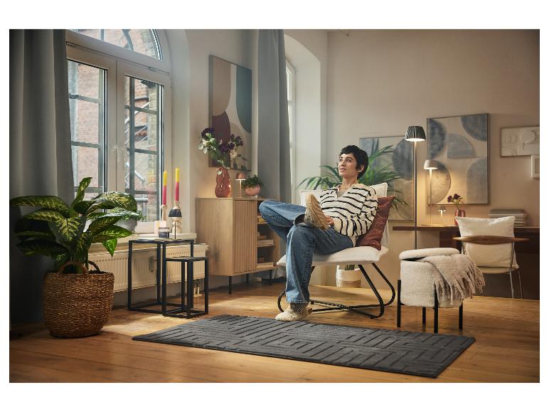 Eine Person entspannt in einem modernen und gemütlichen Wohnzimmer auf einem Sessel.