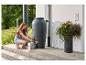 Frau füllt Gießkanne aus einer Regentonne im Garten.