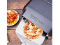 Pizzaofen mit frischer Pizza auf einem Pizzaschieber, daneben Kirschtomaten.