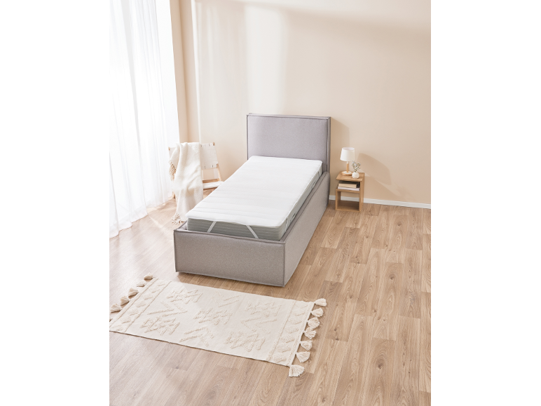 Graues Boxspringbett mit weißer Matratze in einem Schlafzimmer mit Holzboden und beigem Teppich.