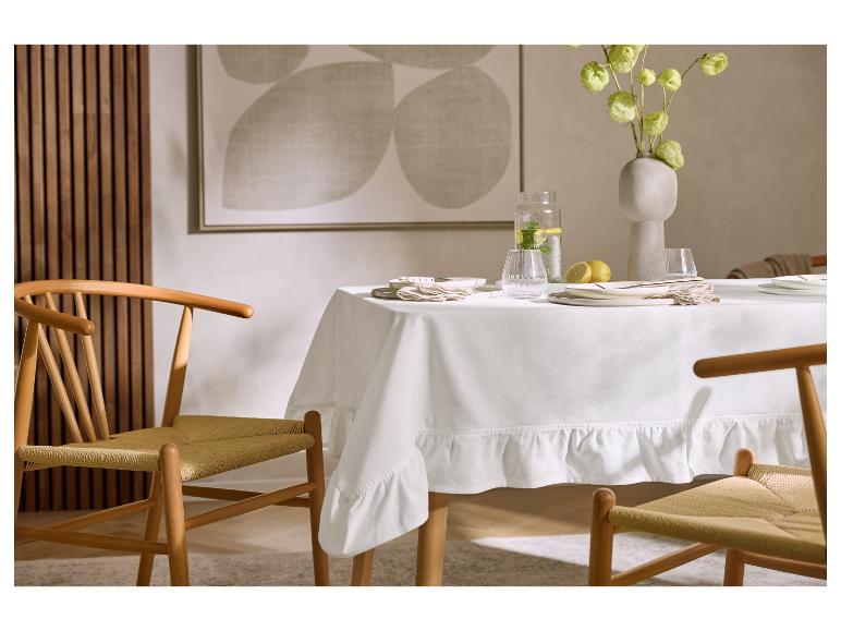 Esstisch mit weißer Tischdecke, Geschirr, Blumenvase und Holzstühlen.