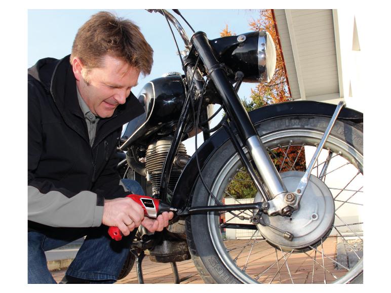 Mann benutzt einen Akkuschrauber, um an einem Oldtimer-Motorrad zu arbeiten.