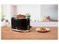 Schwarzer Toaster mit zwei Scheiben Brot, daneben ein Teller mit einem Tomatenbrot.