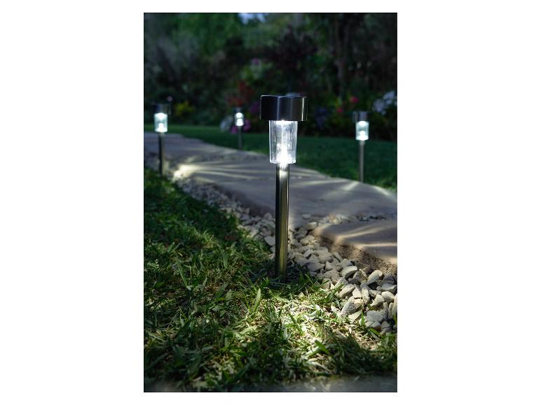 Solarbetriebene Gartenwegleuchten beleuchten einen Steinweg in der Dämmerung.