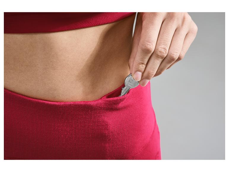 Eine Hand steckt einen Schlüssel in die Tasche einer rosafarbenen Hose.