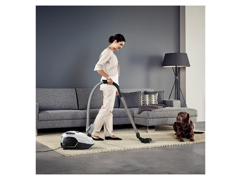 Frau staubsaugt im Wohnzimmer, Hund liegt auf dem Teppich.