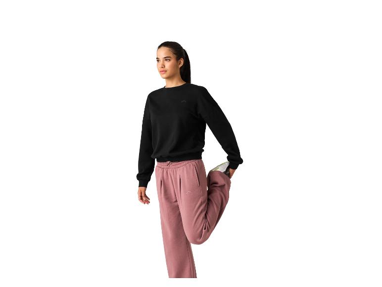 Frau in schwarzem Sweatshirt und rosa Jogginghose, die sich dehnt.