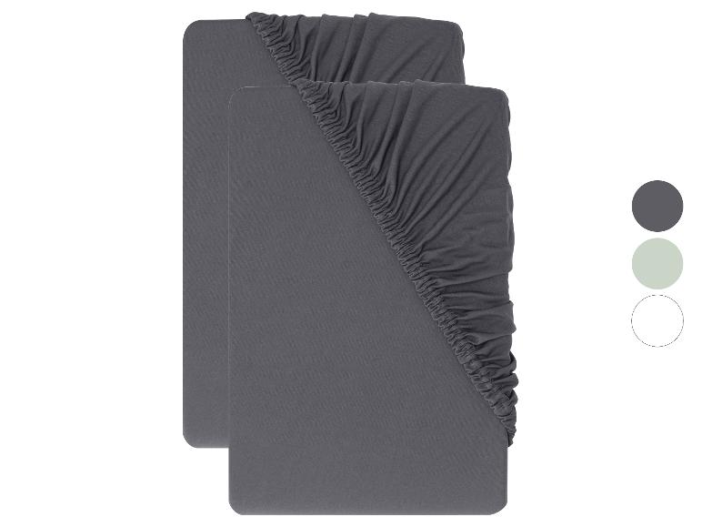 Zwei graue Spannbettlaken mit Gummizug an den Ecken, mit Farbmustern in Grau, Hellgrün und Weiß.