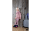 Lächelndes Mädchen in rosa Strickpullover und Hose, an eine Holzwand gelehnt.