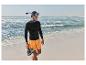 Mann in schwarzem Rashguard und orangefarbenen Shorts mit Schnorchelmaske und Wasserschuhen am Strand