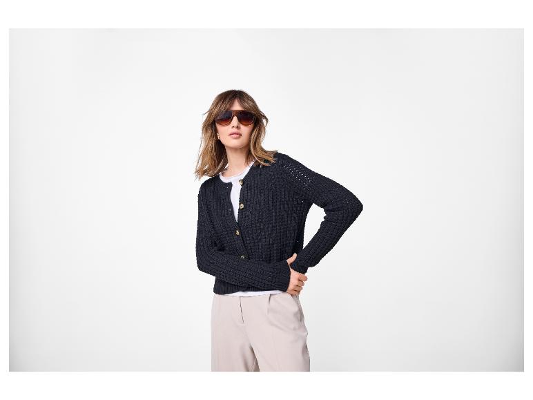 Frau in schwarzer Strickjacke, weißem T-Shirt und beiger Hose, mit Sonnenbrille