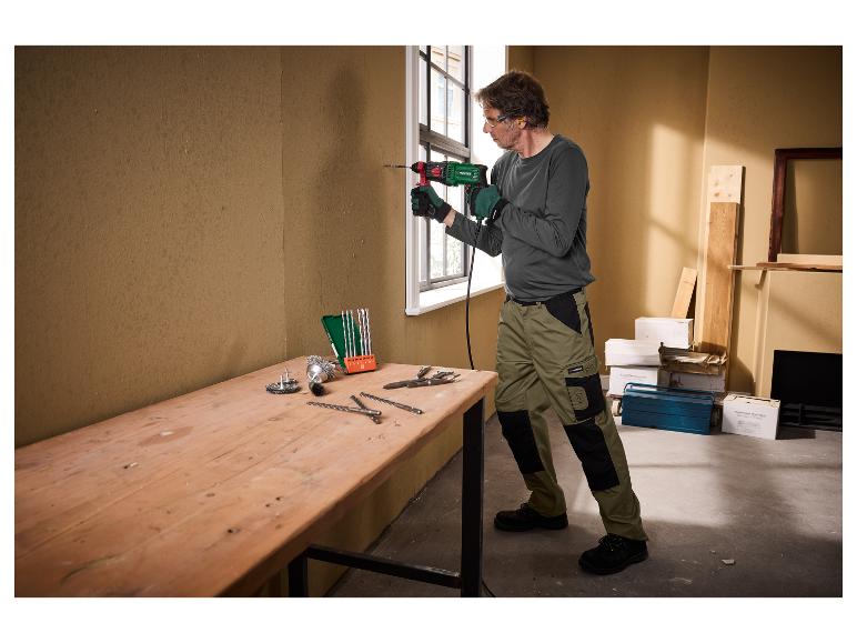 Mann mit Handschuhen und Schutzbrille bohrt eine Wand mit einem Parkside Bohrer.