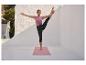 Frau macht Yoga im Freien, trägt ein lila Top und schwarze Capri-Leggings, auf einer rosa Yogamatte.