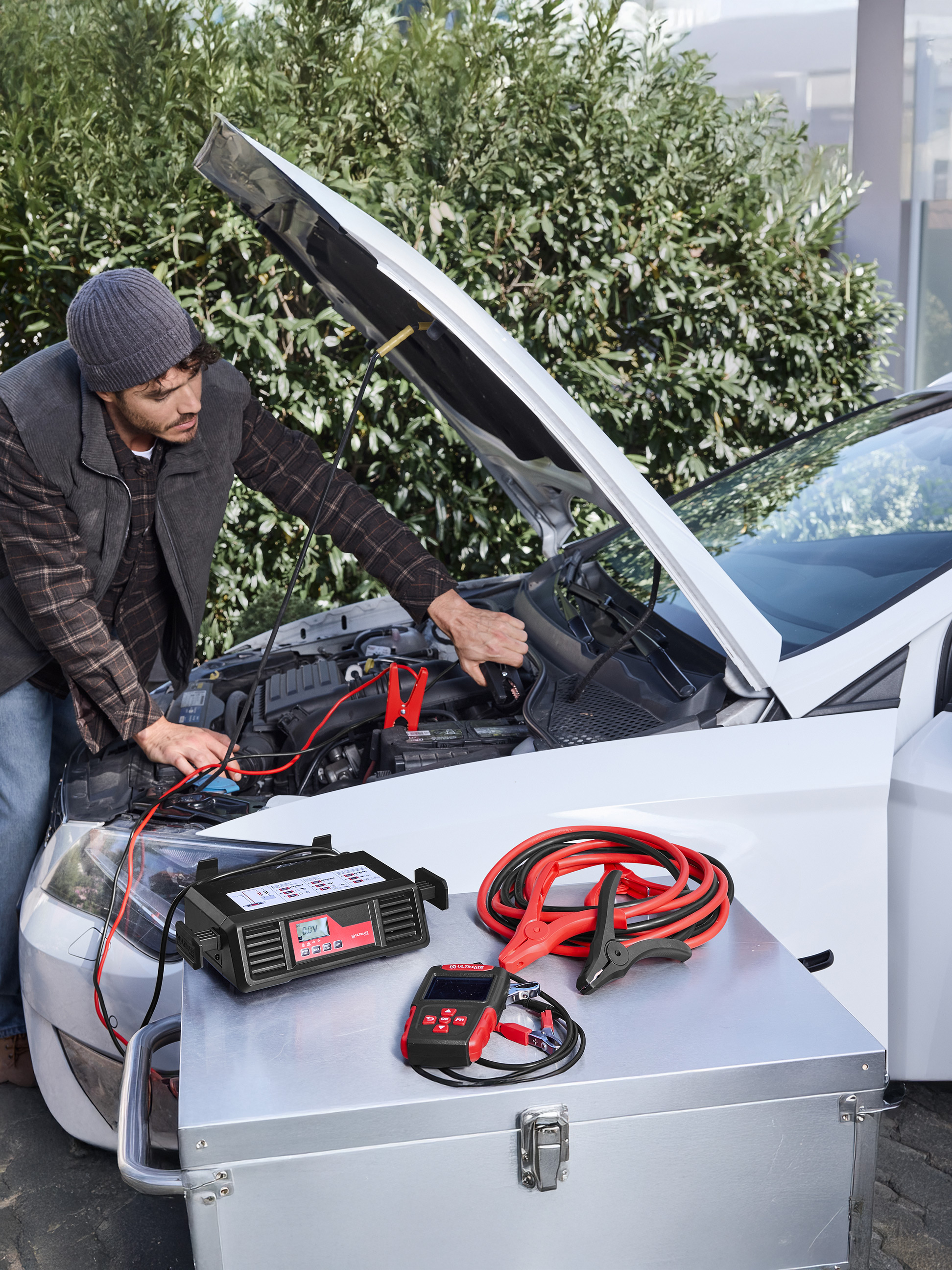 Mann benutzt ULTIMATE SPEED Autobatterieladegerät und Überbrückungskabel an einem Auto.