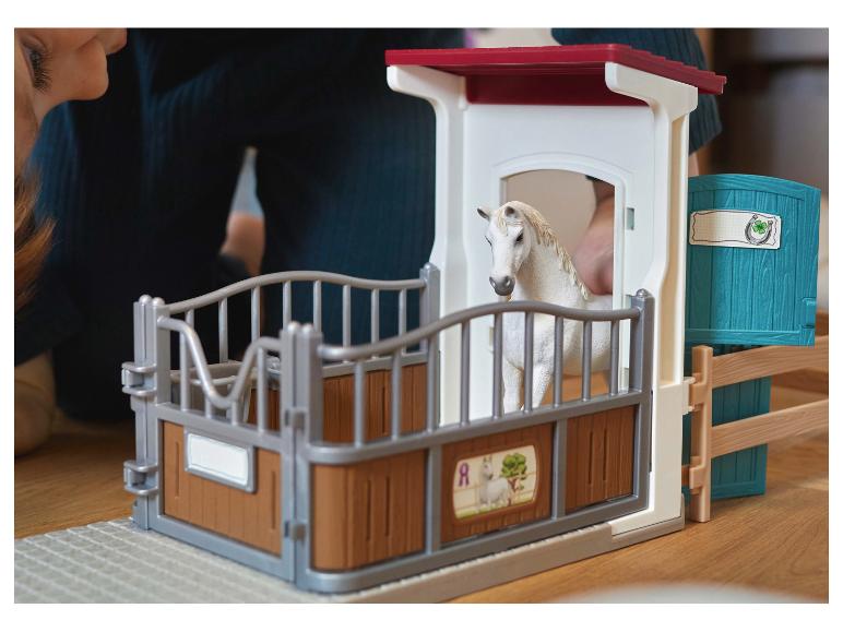 Kind spielt mit einem Spielzeug-Pferdestall mit einem weißen Pferd.
