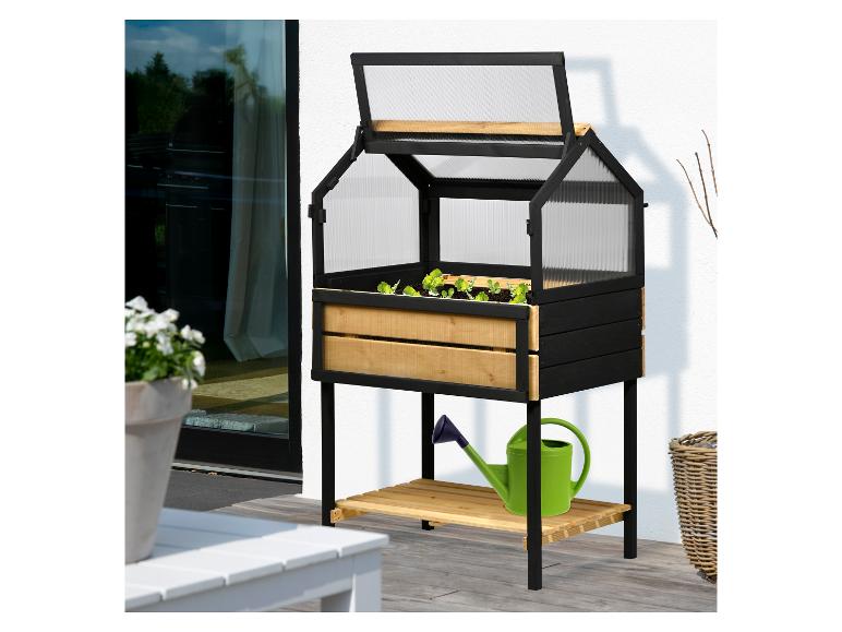 Erhöhtes Mini-Gewächshaus aus schwarzem und Naturholz mit Pflanzen und grüner Gießkanne auf Terrasse.