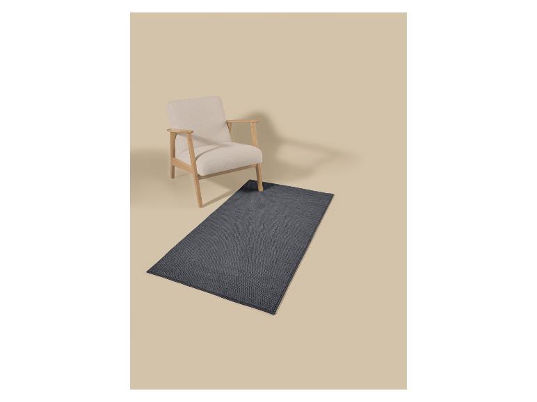 Heller Holz-Sessel mit beigen Kissen und einem dunkelgrauen rechteckigen Teppich.