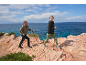 Zwei Wanderer mit Trekkingstöcken an einer felsigen Küste am Meer.