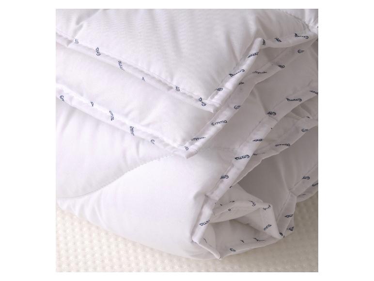 Gefaltete weiße Bettdecke mit Steppnähten und wiederholtem Textmuster.