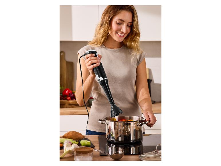 Frau benutzt einen Stabmixer in einem Topf mit Gemüse auf einem Kochfeld.