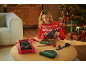 Frau im Weihnachtspullover benutzt Heißklebepistole zum Geschenke einpacken, mit Mützen auf dem Tisch.
