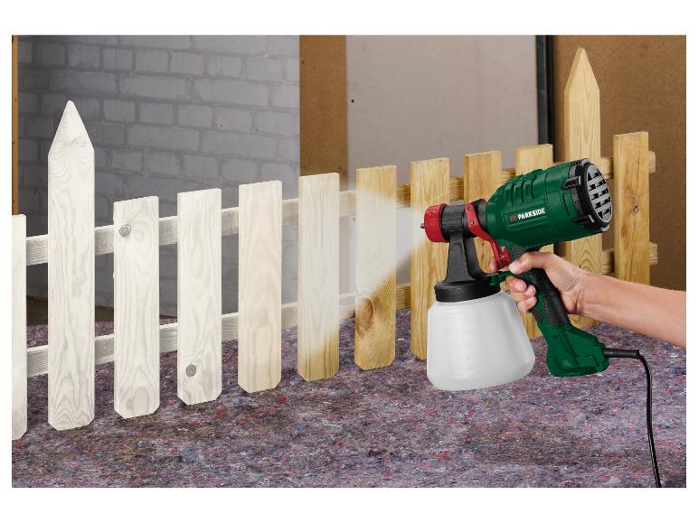 Person streicht einen Holzzaun weiß mit einem Parkside Farbsprühgerät.