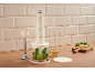Cremefarbener Stabmixer mit Kräutern, Öl und Käse auf einer Holzoberfläche.