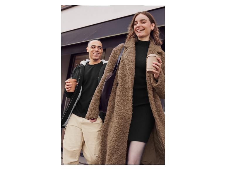 Eine Frau in einem braunen Teddyfellmantel und ein Mann in einer schwarzen Jacke gehen die Straße entlang.