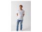 Mann in weißem T-Shirt mit Aufschrift und blauen Jeans, Hände in den Taschen.
