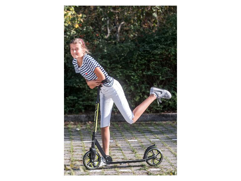 Lächelndes Mädchen in gestreiftem T-Shirt und weißer Hose, posiert mit einem Roller.